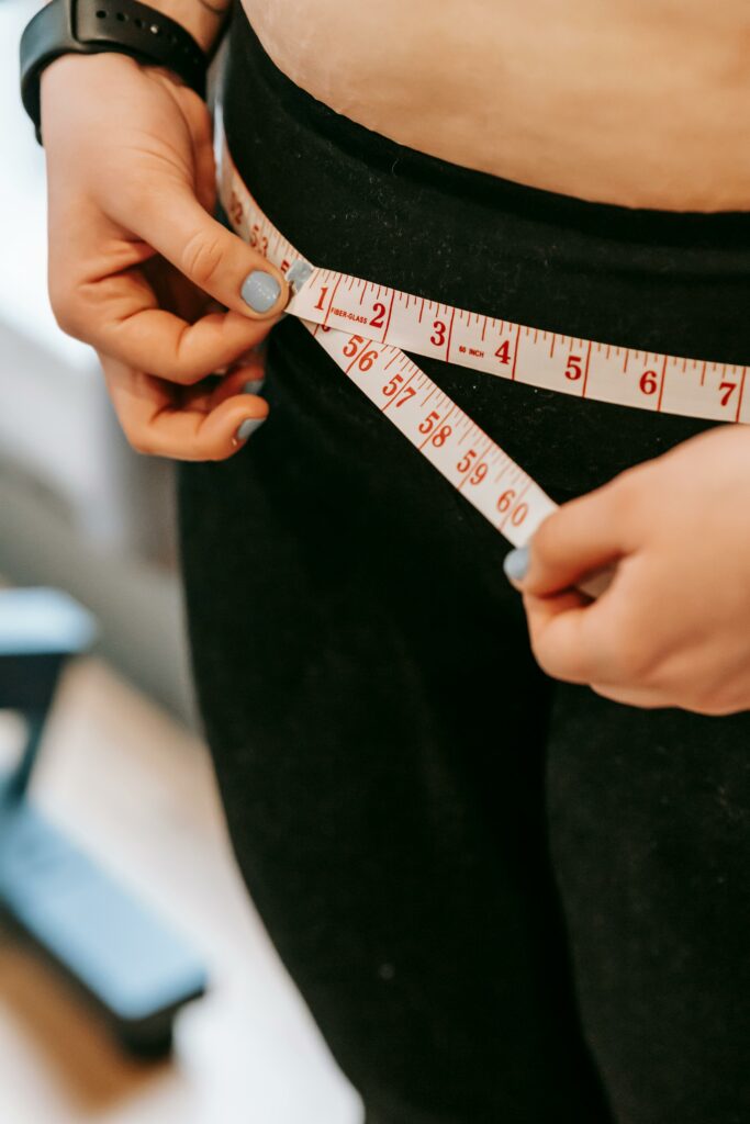 From above of crop anonymous plump female using measuring tape around hips in gym